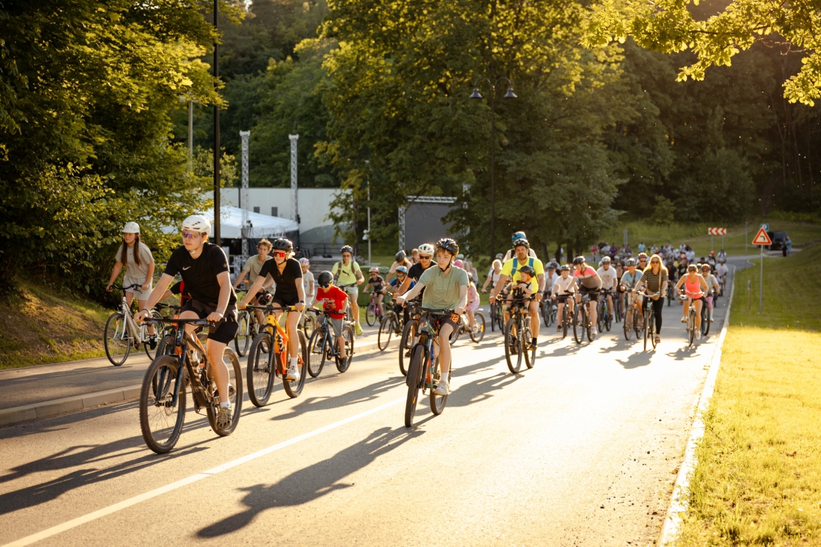 Plaša velobraucēju grupa brauc pa saules apspīdētu ceļu