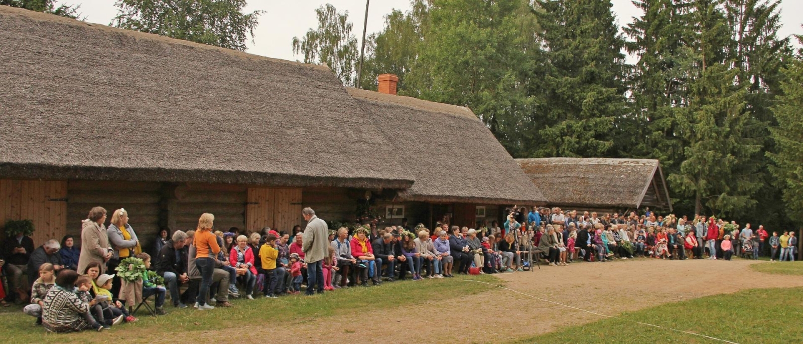 Cilvēki pie lauku sētas ēkas
