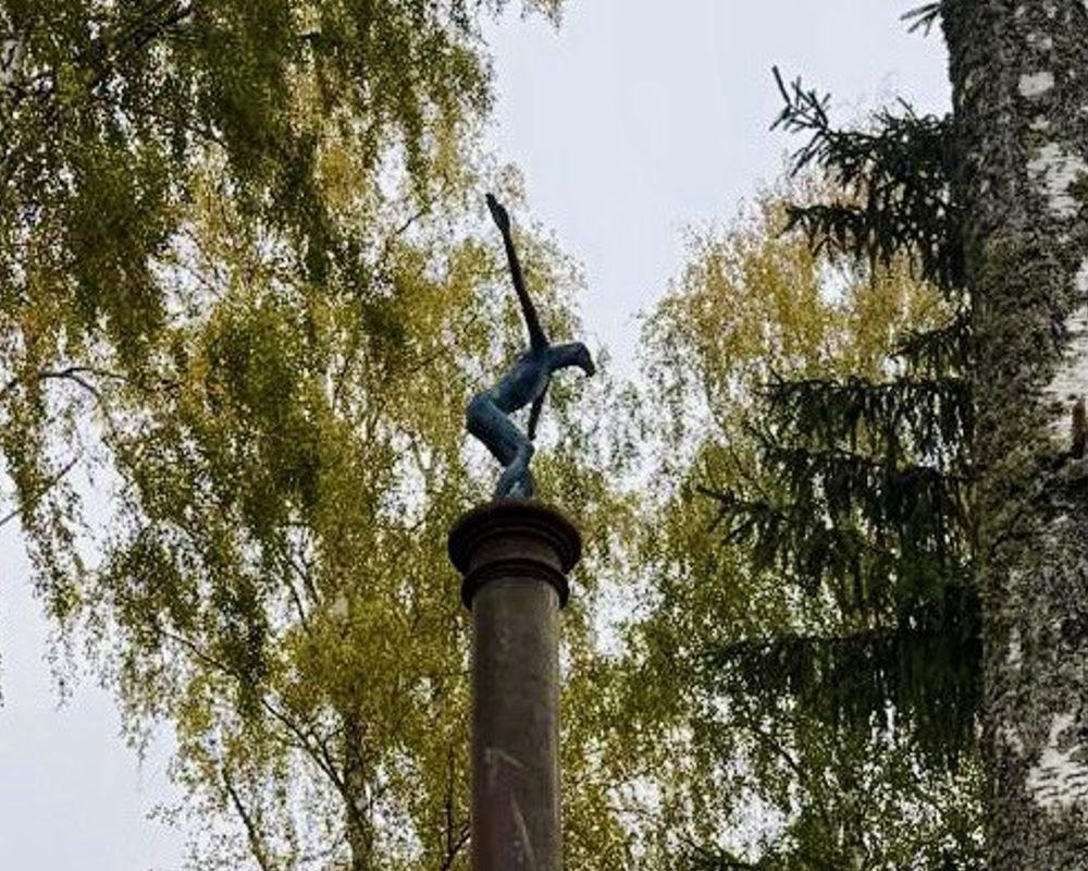 Skulptūra uz kolonnas starp kokiem